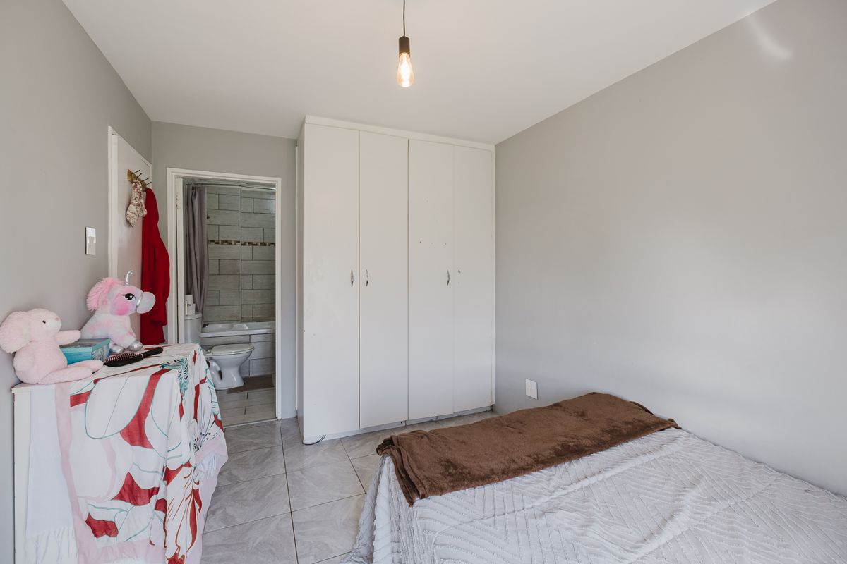 A bedroom featuring tiled flooring, built-in cupboards, and an en-suite bathroom with a bathtub.