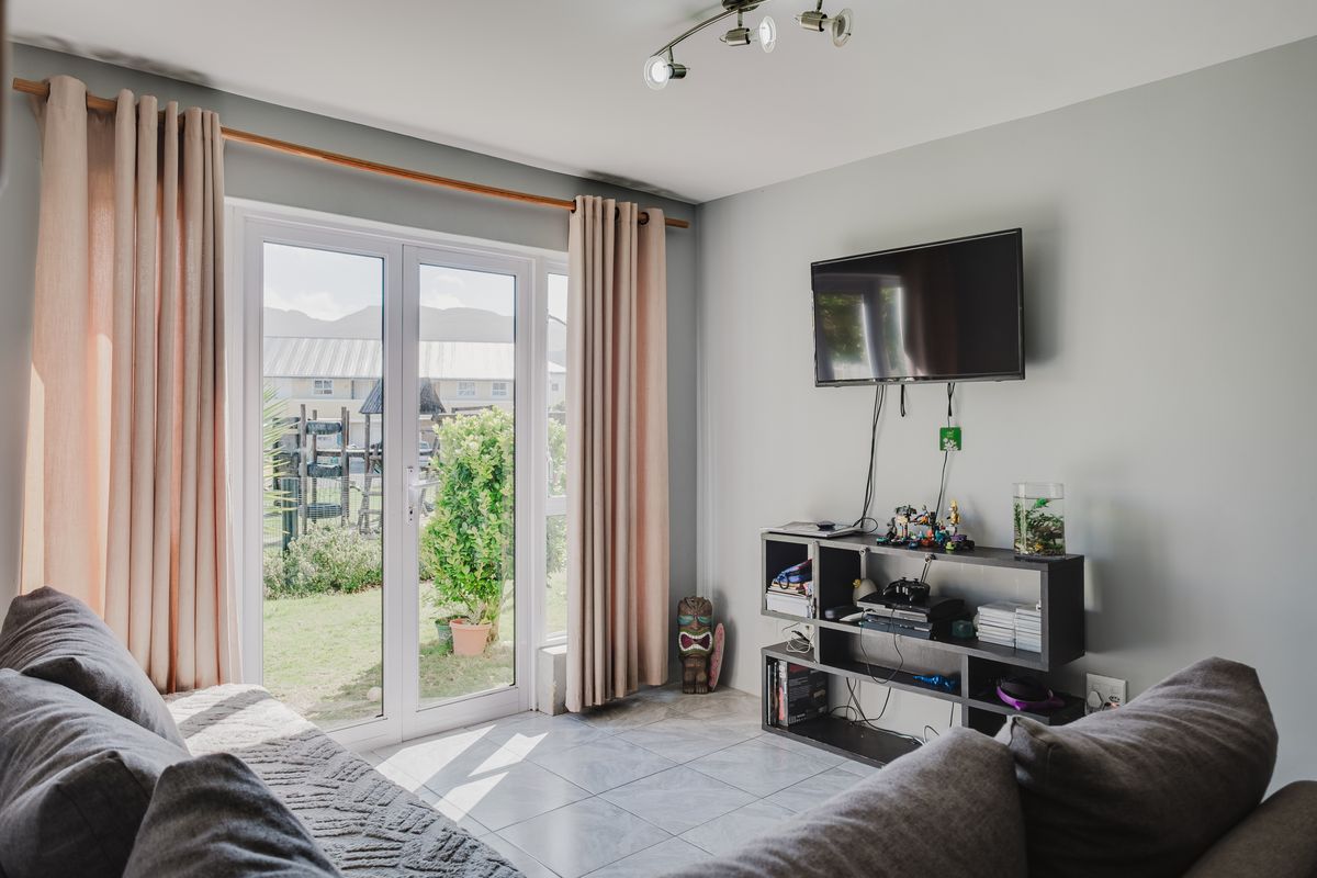 A bright living room featuring tiled flooring and double french doors providing direct access to the rear garden area.