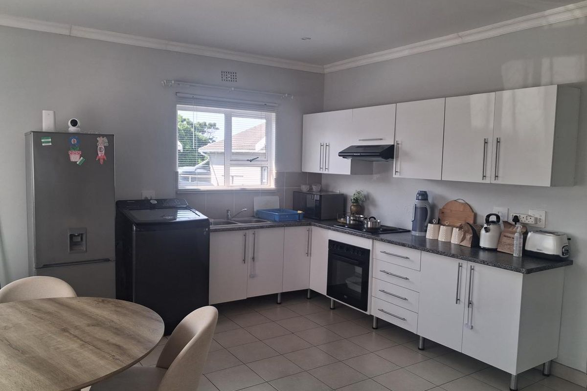 A functional kitchen featuring white cabinetry, dark laminate countertops, built-in oven with hob, and tiled flooring, offering a clean and practical workspace.
