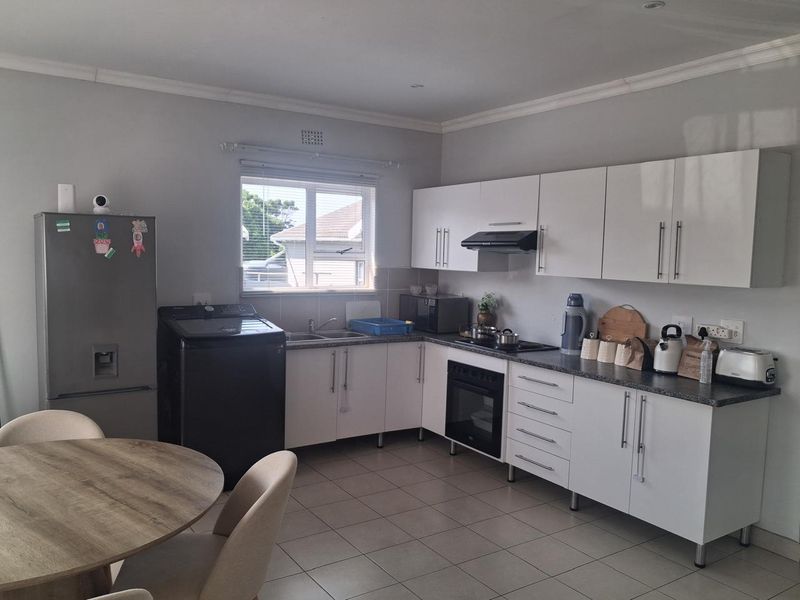 A functional kitchen featuring white cabinetry, dark laminate countertops, built-in oven with hob, and tiled flooring, offering a clean and practical workspace.