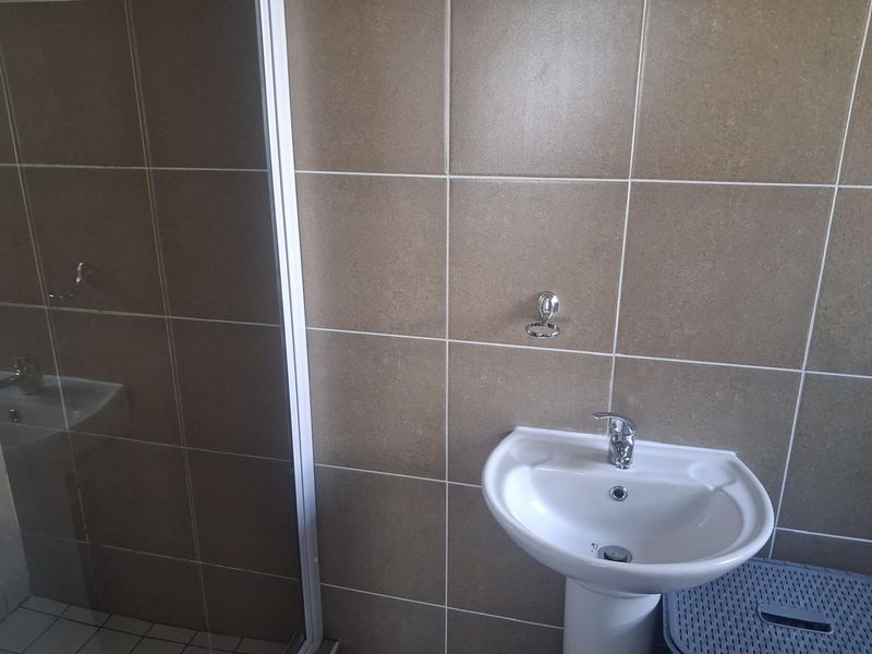 A functional bathroom featuring a pedestal basin with a chrome mixer tap and a glass-enclosed shower with neutral wall tiling.