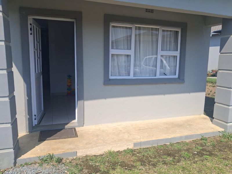 Front entrance of the townhouse featuring a concrete porch, aluminium window frames, and a neutral grey exterior facade.