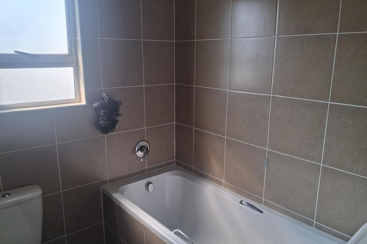 A functional bathroom featuring a bathtub with a mixer tap, a toilet, and neutral wall tiling, complemented by a frosted window for privacy.