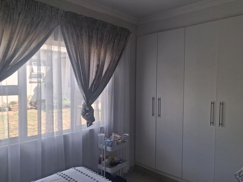 A bedroom featuring built-in cupboards and a large window with natural light, overlooking the exterior garden area.