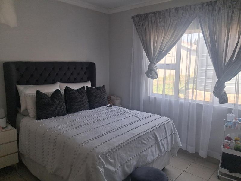 A well-maintained bedroom featuring tiled flooring, neutral wall tones, and a large window allowing for natural light.