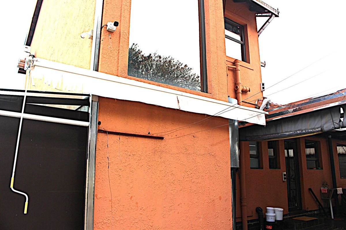 Rear exterior view of the property showing textured orange facade, large fixed windows, and an attached awning structure with visible maintenance requirements.