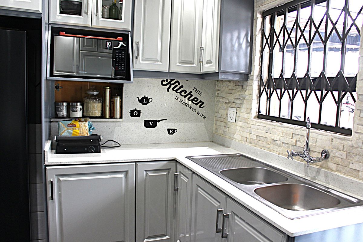 A well-maintained kitchen featuring grey and white cabinetry, stone countertops, a double stainless steel sink, and a decorative stone-clad backsplash.