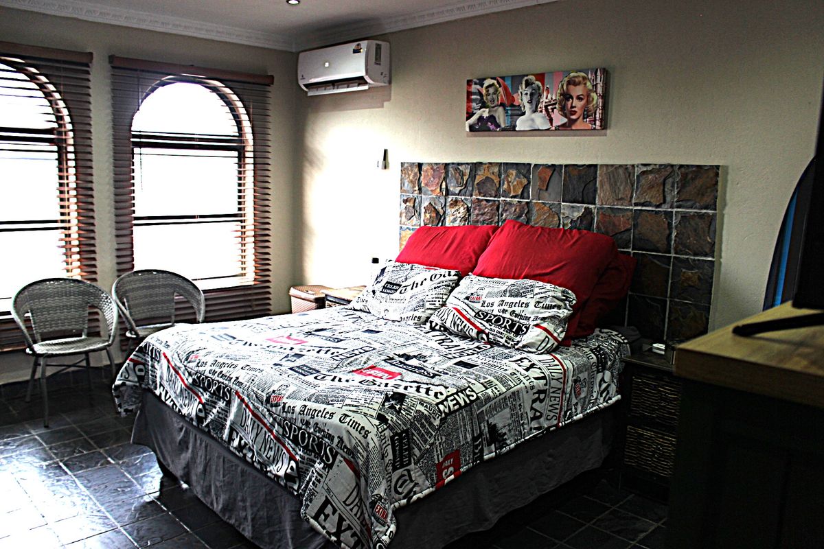 A bedroom featuring a stone accent wall, tiled flooring, arched windows with venetian blinds, and a wall-mounted air conditioning unit.