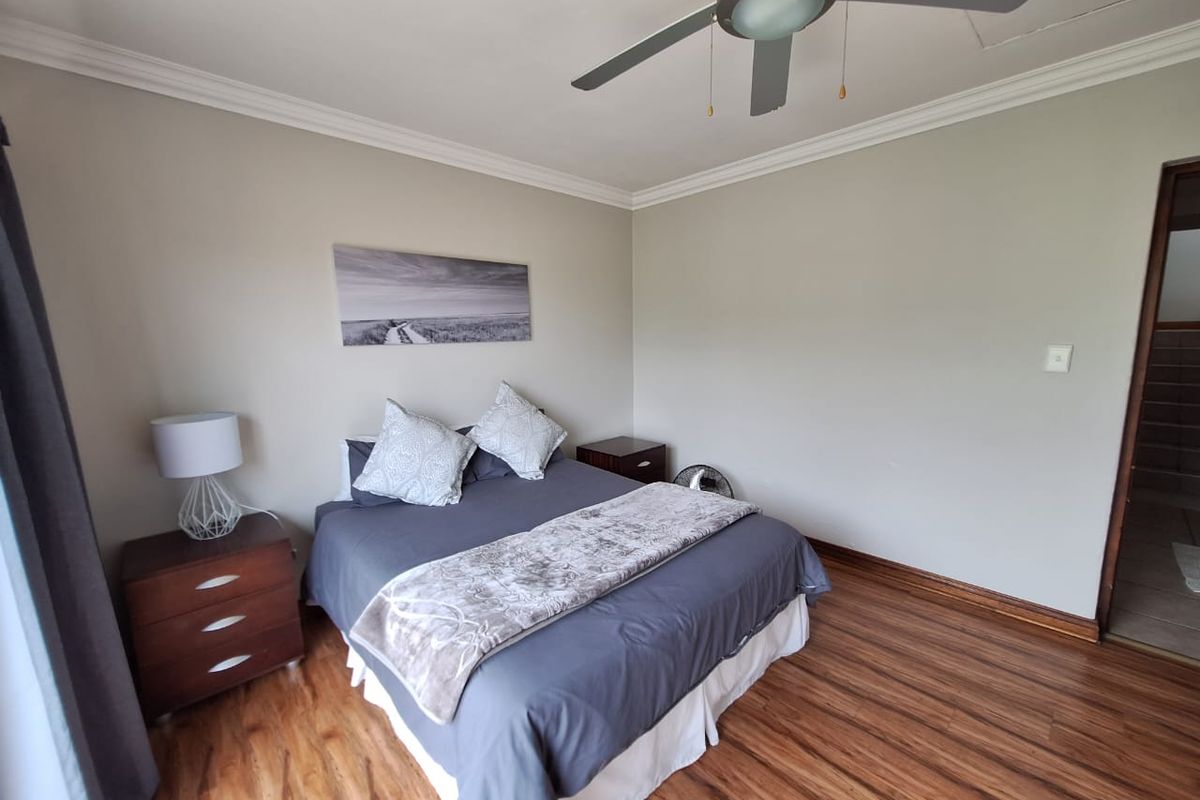 A well-maintained bedroom featuring laminate flooring, crown molding, and a ceiling fan, offering a clean and neutral living space.