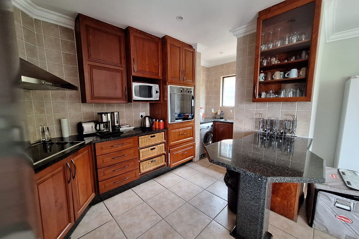 A functional kitchen featuring warm-toned wooden cabinetry, granite countertops, a breakfast bar, and integrated appliances with tiled flooring and backsplash.