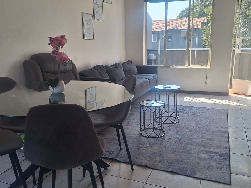 An open-plan living and dining area featuring tiled flooring, large windows for natural light, and direct access to an outdoor balcony space.