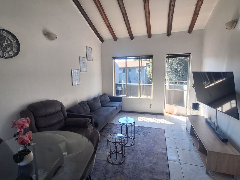 A living room featuring exposed timber ceiling beams, tiled flooring, and direct access to an outdoor balcony area through a sliding glass door.