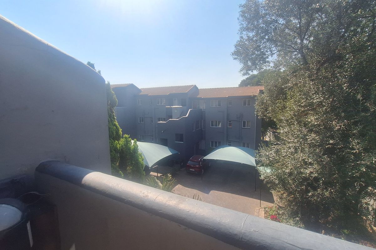 View from an elevated balcony overlooking the apartment complex parking area with shade cloth carports and mature trees.