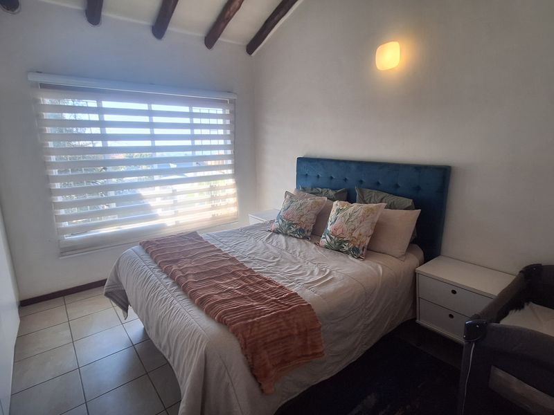 A cozy bedroom featuring exposed timber ceiling beams, tiled flooring, a built-in wardrobe, and a window with modern roller blinds.