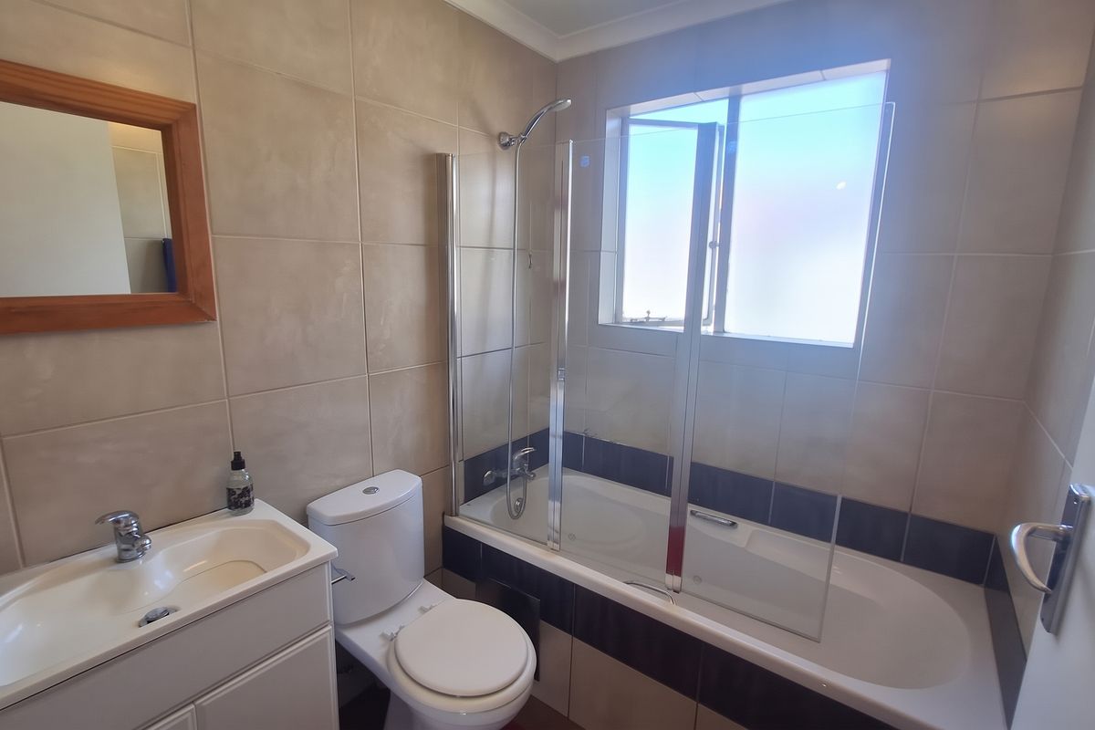 A functional bathroom featuring a vanity with basin, a toilet, and a bathtub with a glass shower screen and tiled wall finishes.