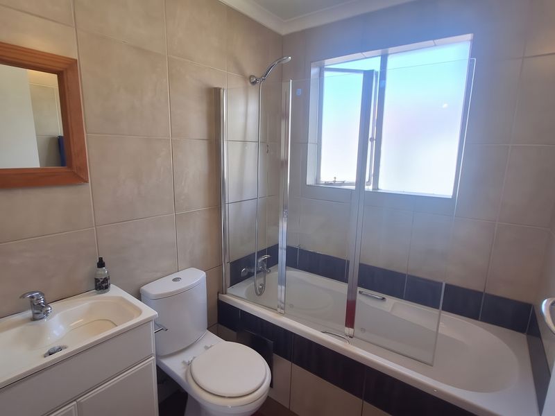 A functional bathroom featuring a vanity with basin, a toilet, and a bathtub with a glass shower screen and tiled wall finishes.