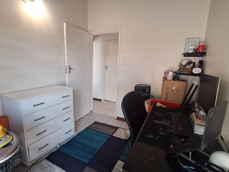 A functional bedroom space featuring tiled flooring and neutral wall finishes, currently utilized as a home office area.