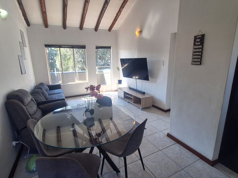 Open-plan living and dining area featuring vaulted ceilings with exposed timber beams, tiled flooring, and large windows providing natural light.