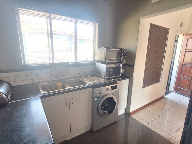 Functional kitchen featuring a double sink, subway tile backsplash, dark laminate countertops, and an integrated washing machine with tiled flooring.