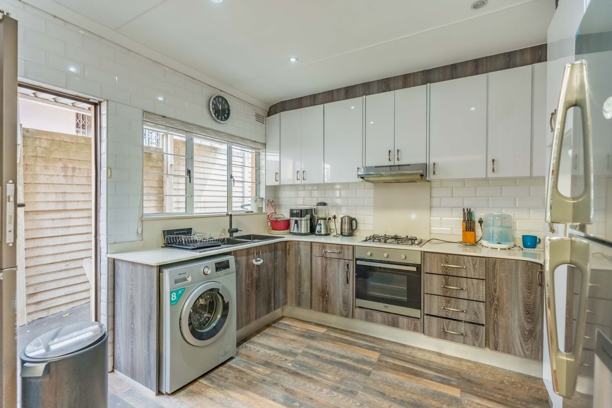 Modern kitchen featuring white and wood-grain cabinetry, subway tile backsplash, gas hob, built-in oven, and integrated laundry appliance space.