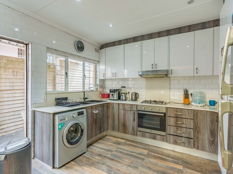 Modern kitchen featuring white and wood-grain cabinetry, subway tile backsplash, gas hob, built-in oven, and integrated laundry appliance space.