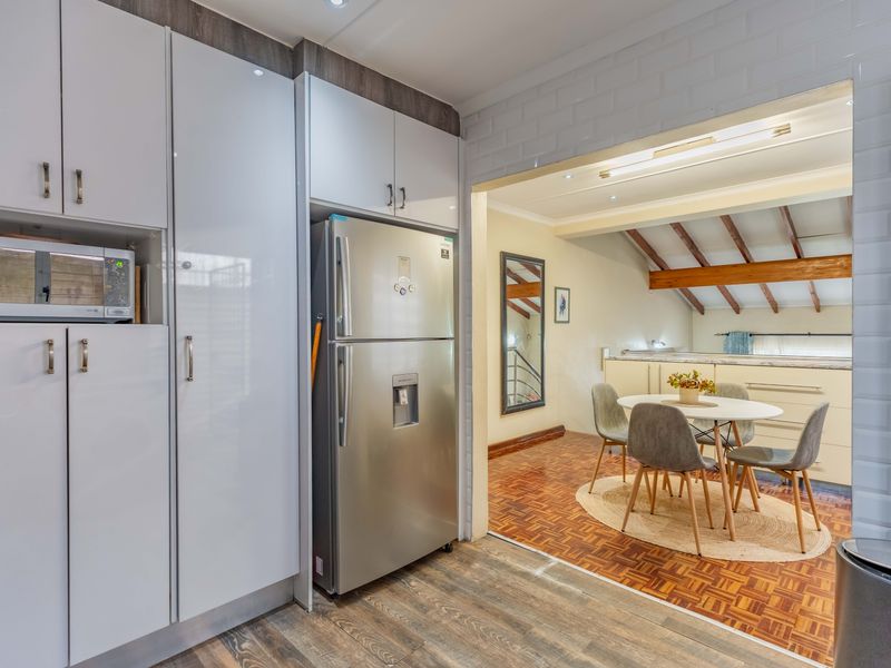 Open-plan kitchen and dining area featuring modern white cabinetry, parquet flooring, and exposed timber ceiling beams, creating a warm and functional living space.