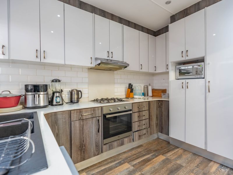 Modern kitchen featuring high-gloss white upper cabinets, wood-grain lower cabinetry, stone countertops, subway tile backsplash, and integrated stainless steel appliances.