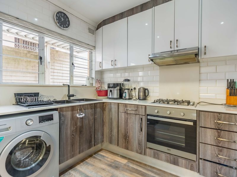 A functional kitchen featuring modern wood-grain cabinetry, white subway tile backsplash, built-in gas hob, oven, extractor fan, and an integrated washing machine.