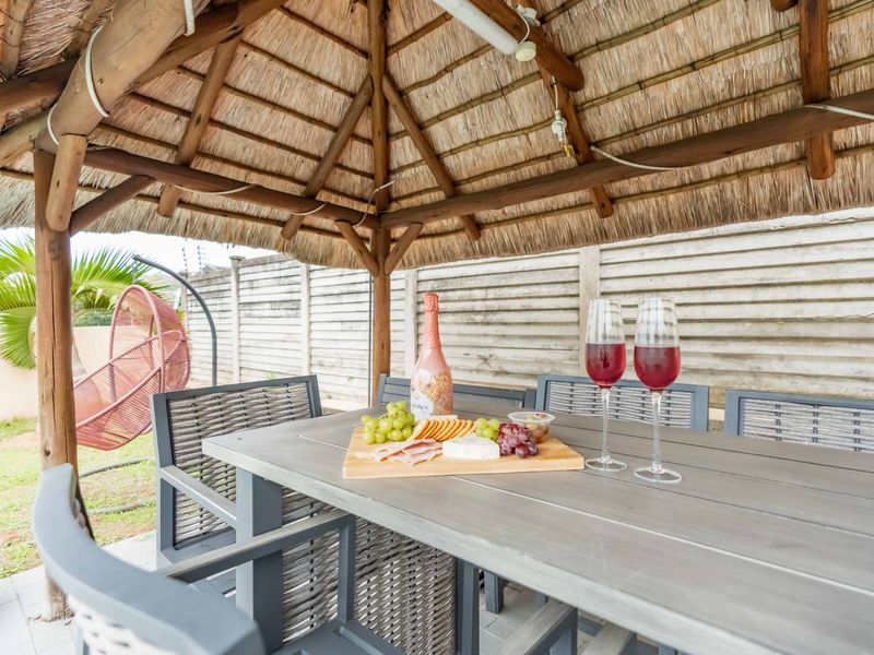 A covered outdoor patio area featuring a traditional thatched roof structure, timber support beams, and paved flooring, enclosed by a precast concrete boundary wall.