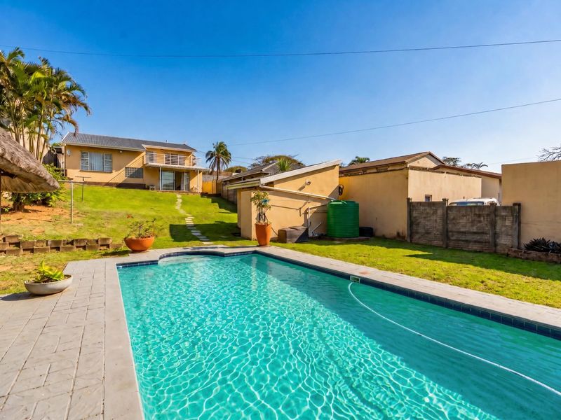 Spacious backyard featuring a swimming pool with paved surround, a sloped lawn, and a water storage tank, set against the rear elevation of the house.