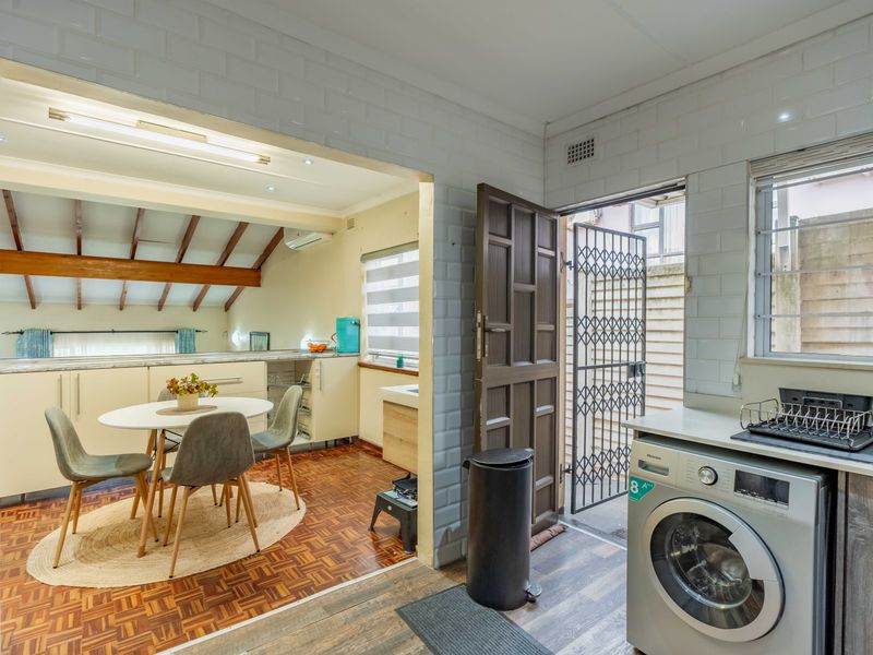 A functional scullery and laundry area featuring subway tile walls, parquet flooring, and direct access to an exterior security gate.