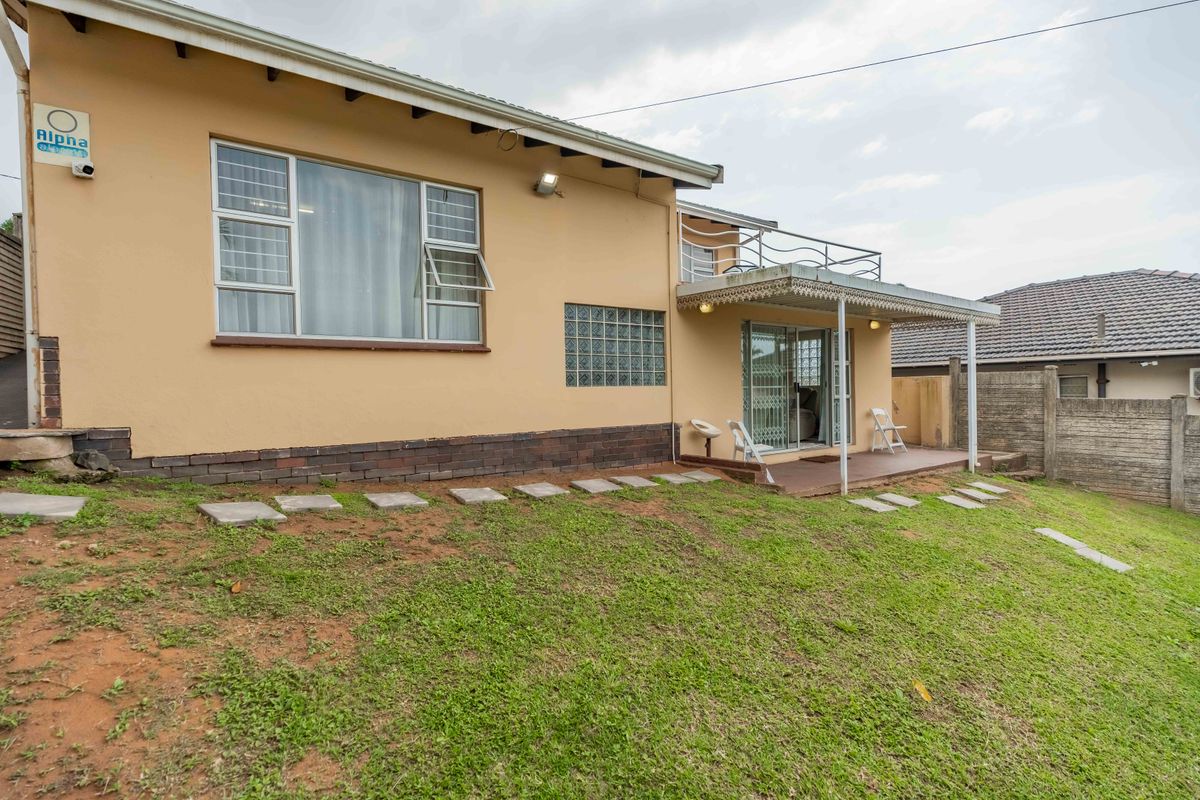 Rear view of the house featuring a covered patio area, sliding glass doors, and a grassed backyard with a brick and plaster exterior finish.