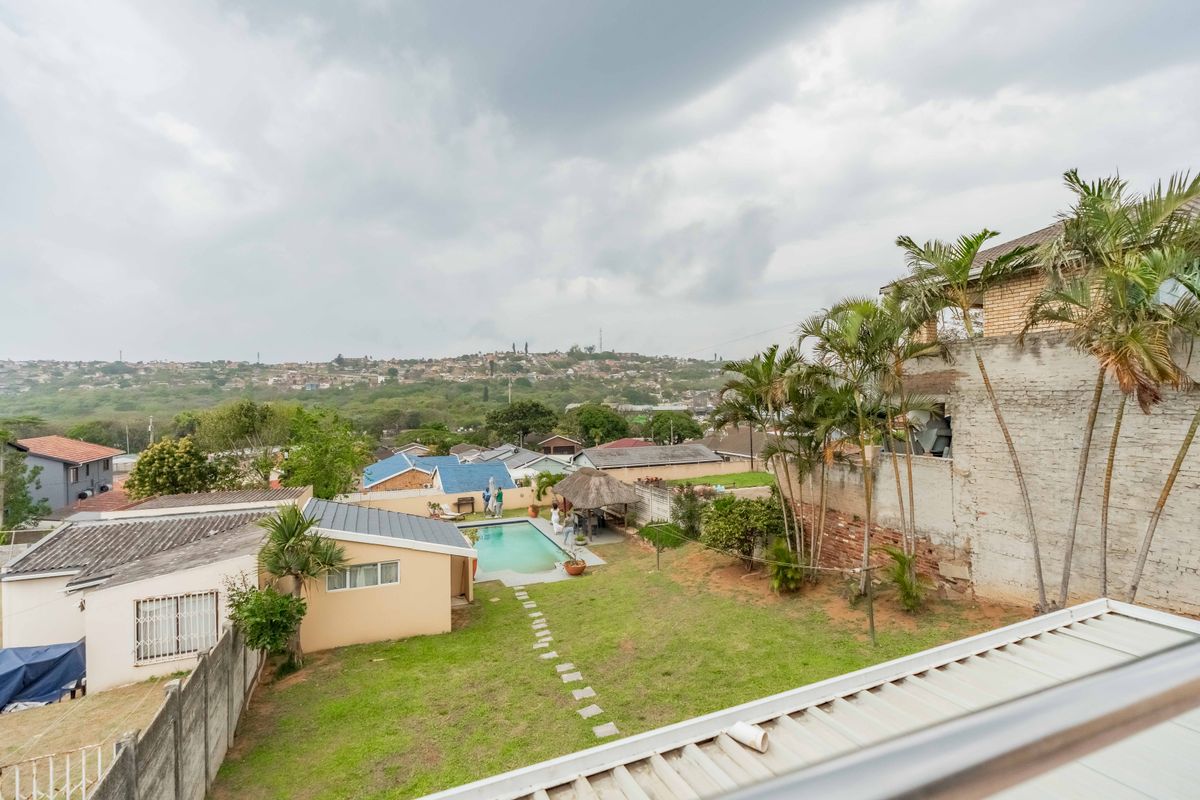 Elevated view of a residential backyard featuring a swimming pool, a thatched gazebo, and a landscaped garden area with surrounding boundary walls.