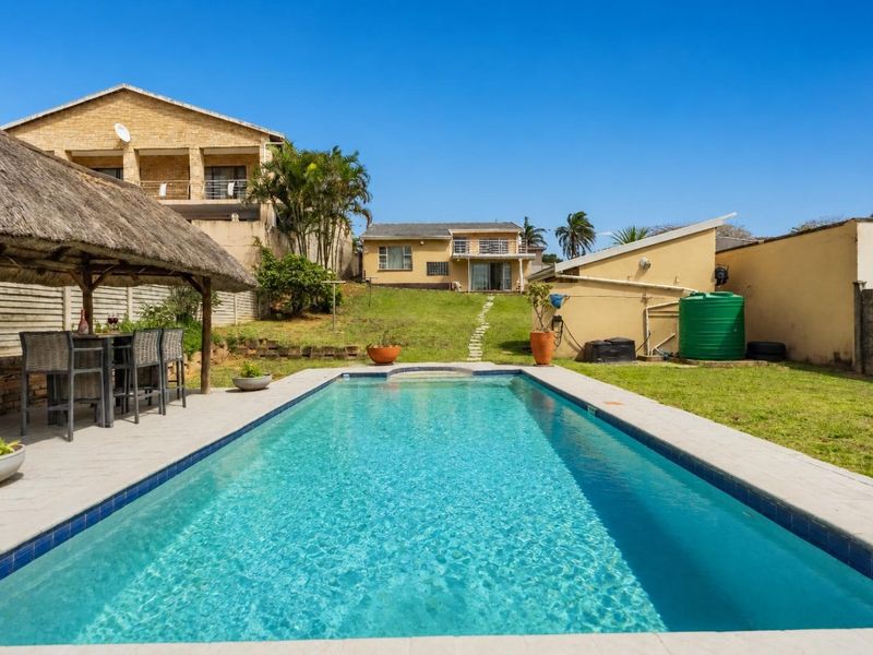 Outdoor pool area featuring a swimming pool, paved surround, and a thatched lapa, set within a spacious garden with a water storage tank.