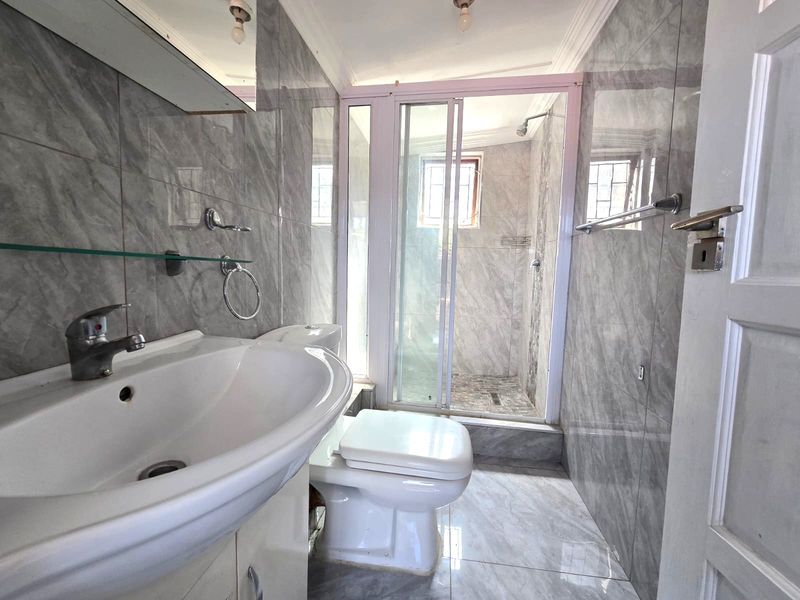 A clean, modern bathroom featuring grey marble-effect wall and floor tiles, a vanity basin, toilet, and a separate glass-enclosed shower.