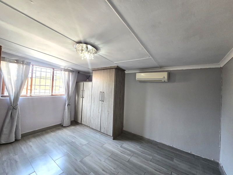 A bedroom featuring tiled flooring, a built-in wardrobe, and a wall-mounted air conditioning unit, providing a functional and neutral living space.