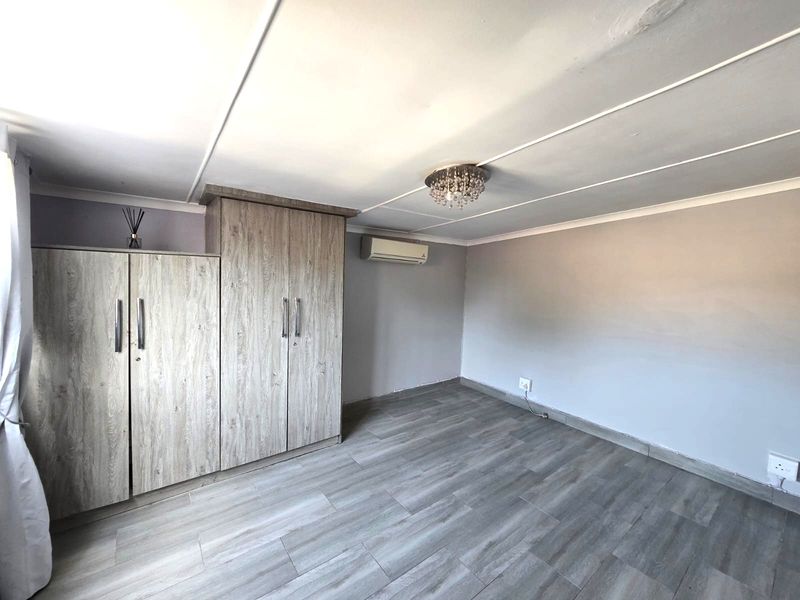 A clean, empty bedroom featuring wood-look laminate flooring, built-in cupboards, and a wall-mounted air conditioning unit.