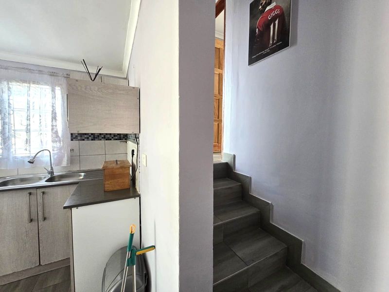 A compact kitchen area featuring built-in cabinetry and a tiled backsplash, adjacent to a staircase with tiled steps.