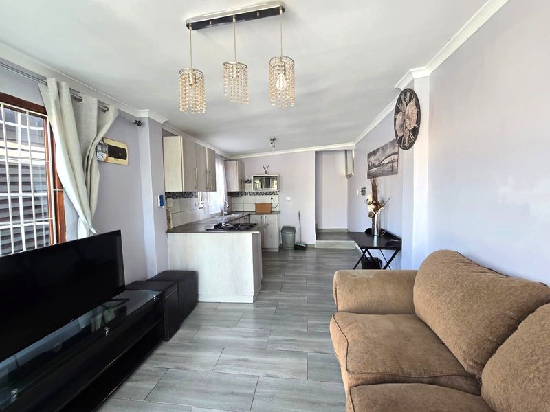 Open-plan living area featuring a modern kitchen with built-in cabinetry, hob, and extractor fan, complemented by tiled flooring throughout the space.
