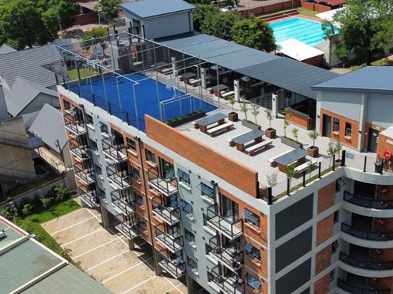 Aerial view of an apartment complex featuring a rooftop sports court, communal terrace area, and private balconies with brick and concrete exterior finishes.