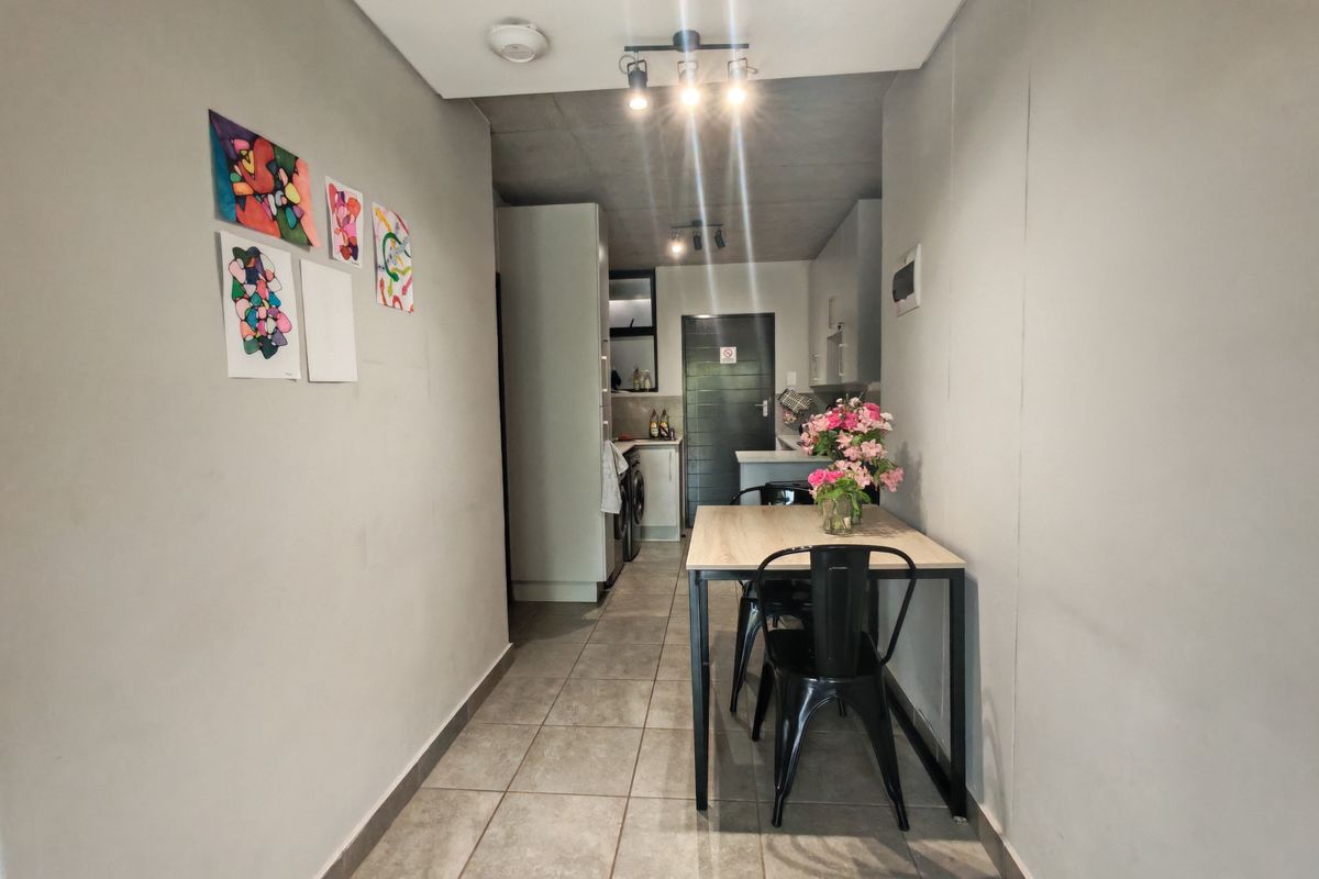 A compact kitchen area featuring tiled flooring, built-in cabinetry, and modern track lighting, leading into a functional utility space.