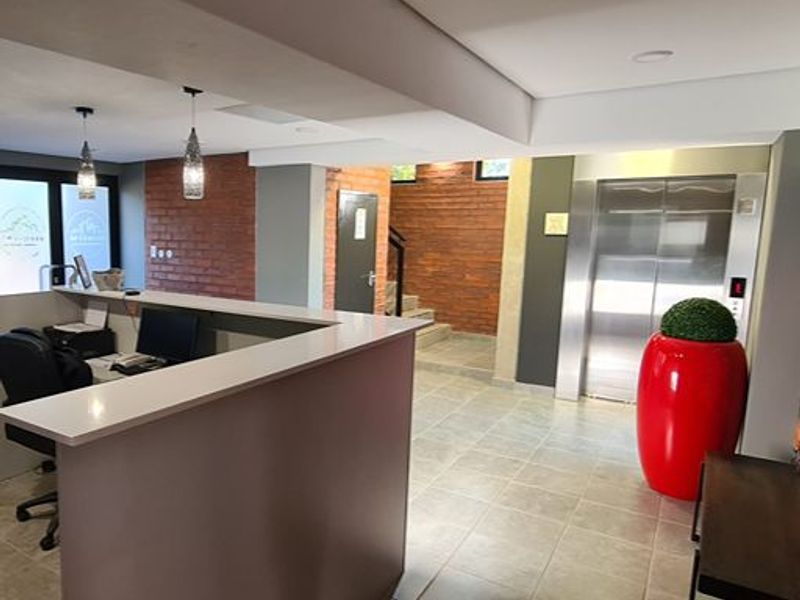 Modern apartment building entrance lobby featuring a reception desk, stainless steel elevator, tiled flooring, and decorative exposed brick wall accents.