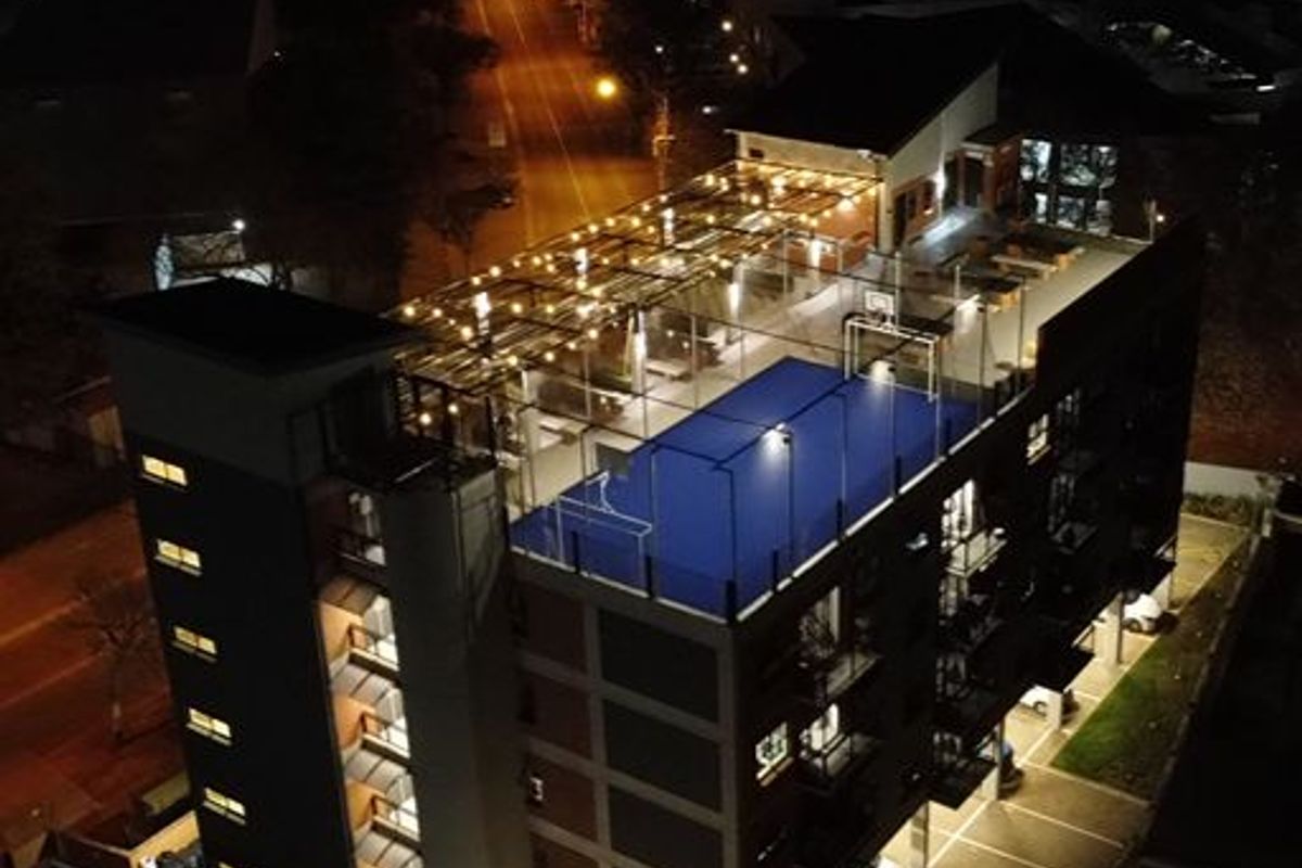 Aerial night view of an apartment building featuring a rooftop sports court, integrated lighting, and ground-level parking facilities.