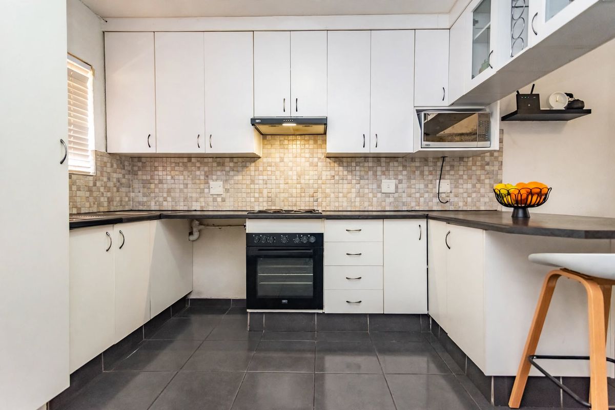 A functional kitchen featuring white cabinetry, mosaic tile backsplash, dark countertops, and integrated appliances including an oven, hob, and microwave.