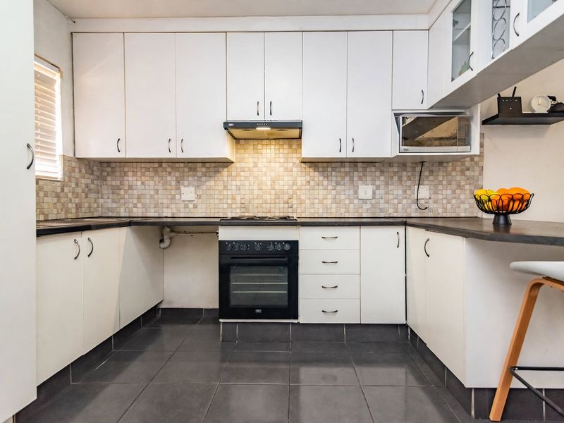 A functional kitchen featuring white cabinetry, mosaic tile backsplash, dark countertops, and integrated appliances including an oven, hob, and microwave.