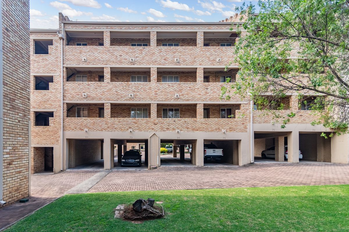 Exterior view of a multi-story apartment building featuring face brick facade, private balconies, and ground-level covered parking bays.