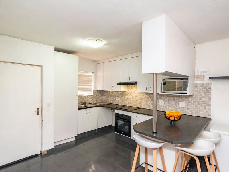 Functional kitchen featuring white cabinetry, dark countertops, a breakfast bar, built-in oven, and tiled backsplash, offering a practical layout for daily cooking.