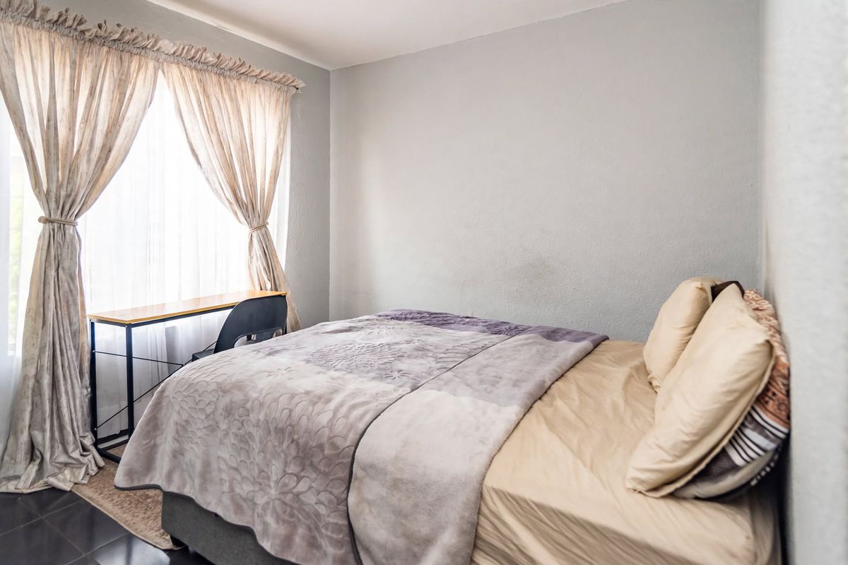 A functional bedroom featuring tiled flooring and natural light through a window with installed curtain rods.