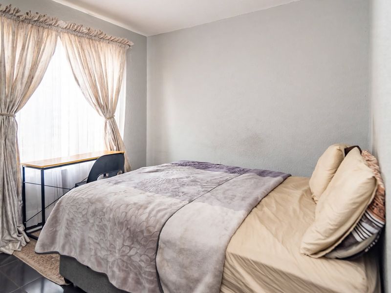 A functional bedroom featuring tiled flooring and natural light through a window with installed curtain rods.