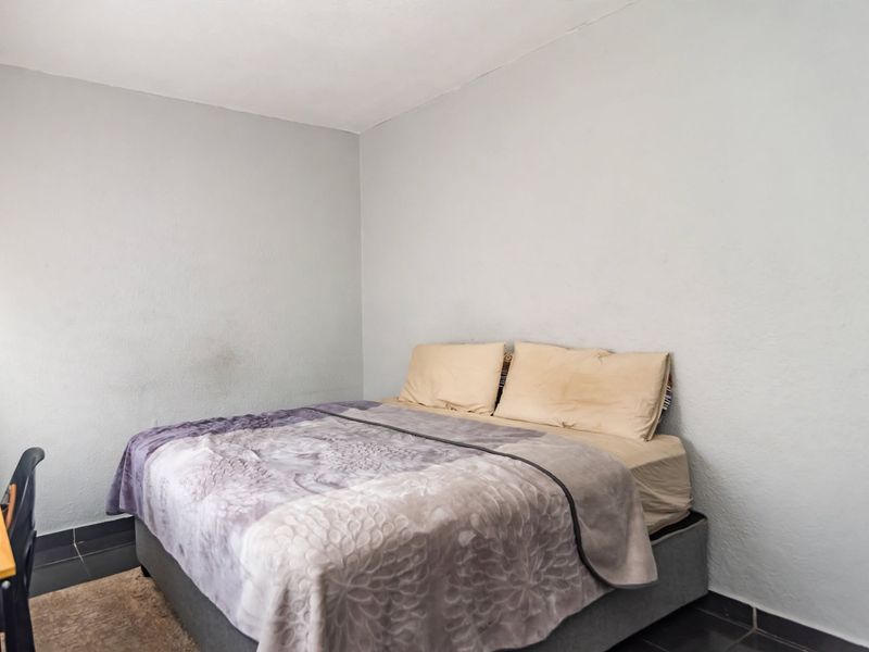 A simple bedroom featuring tiled flooring and neutral wall finishes, providing a functional space ready for cosmetic updates.